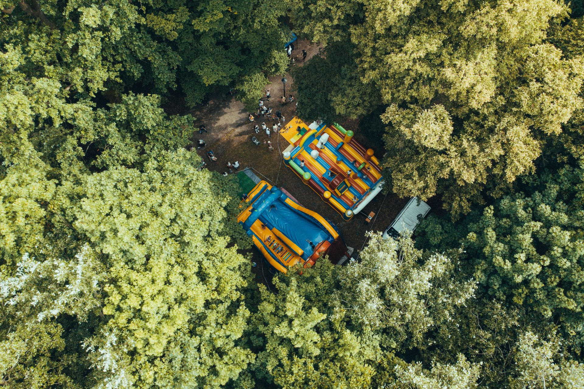 Aerial view of vibrant inflatable play structures nestled in a lush forest setting, with groups of children visible.